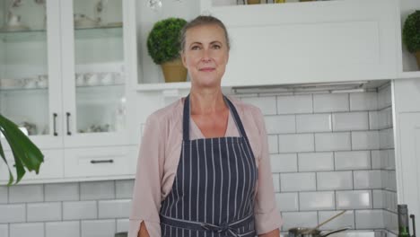 retrato de una mujer caucásica mayor feliz con un delantal azul en la cocina