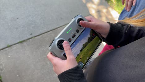 little kid boy or girl flying drone at wide open park with people flying kite being filmed as focus is on small child tiny hands with parent dad in red pants standing to side - in 4k 60fps