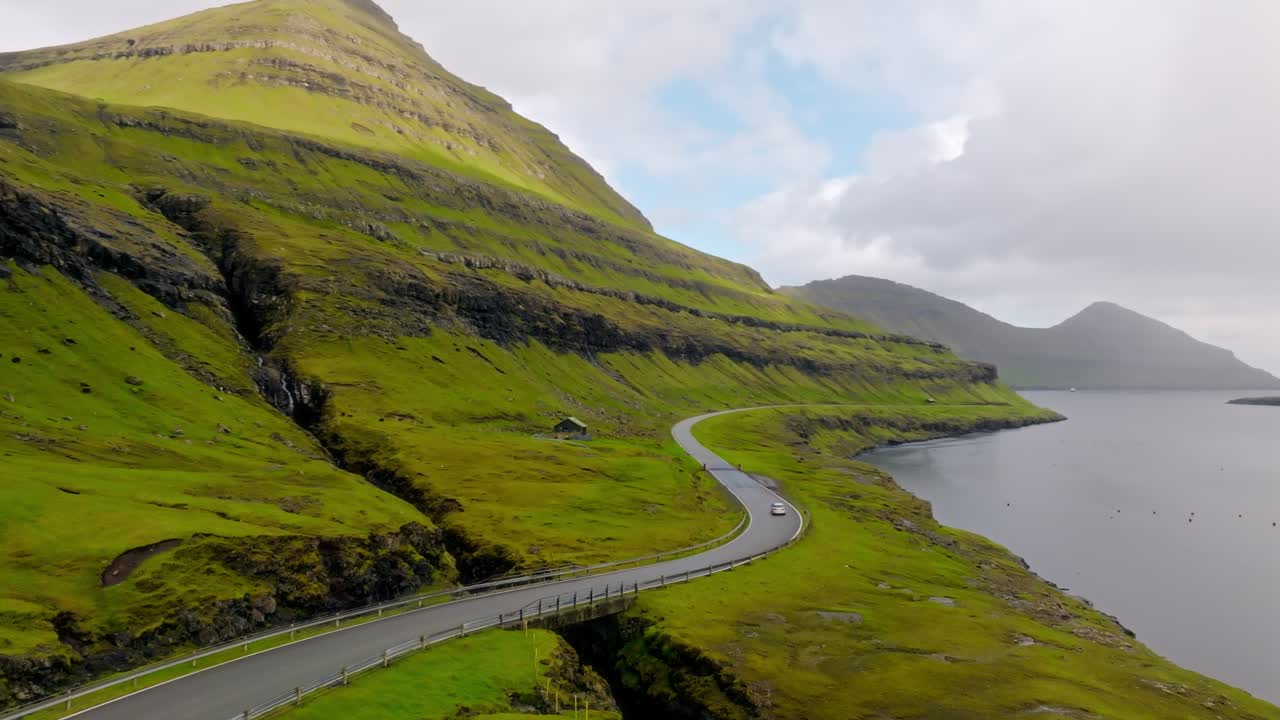 A scenic mountain road winds through the lush green landscape of the Faroe Islands