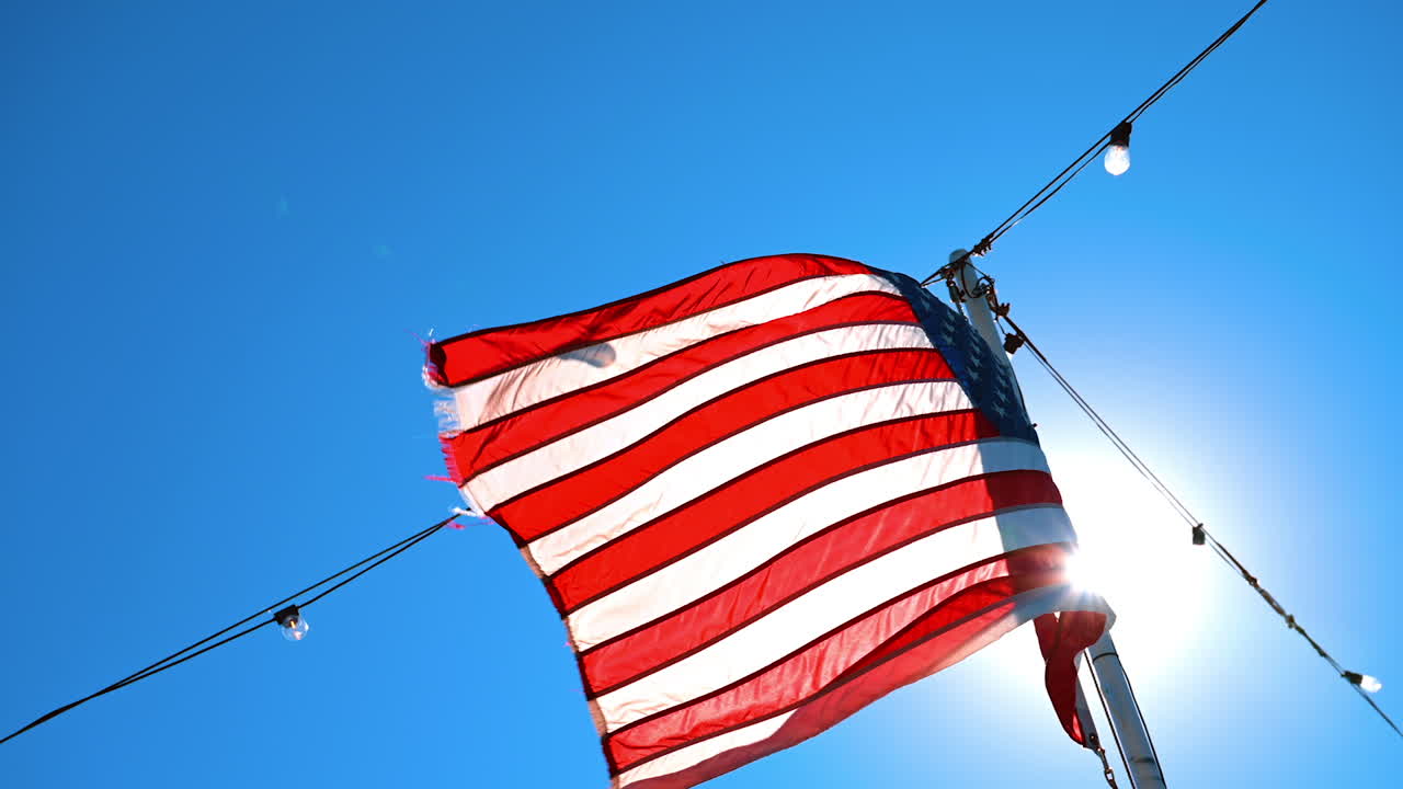 American flag flapping in the wind against clear blue sky. Low angle view. Light bulbs garland hang beside