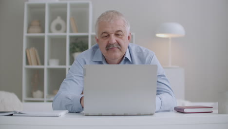 Ein-älterer-Mann-Mit-Schnurrbart-Arbeitet-Mit-Einem-Laptop,-Sitzt-Im-Zimmer-Und-Antwortet-Auf-E-Mails,-Tippt-Den-Text-Einer-Nachricht-Und-Arbeitet-Von-Zu-Hause-Aus