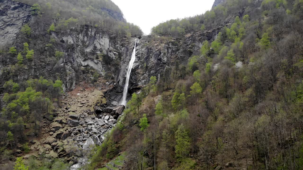 Sorvolo aereo sul paesaggio alpino primaverile di Foroglio in Ticino, Svizzera, con la scena che rivela i tetti delle antiche case in pietra nel villaggio vicino alla cascata.