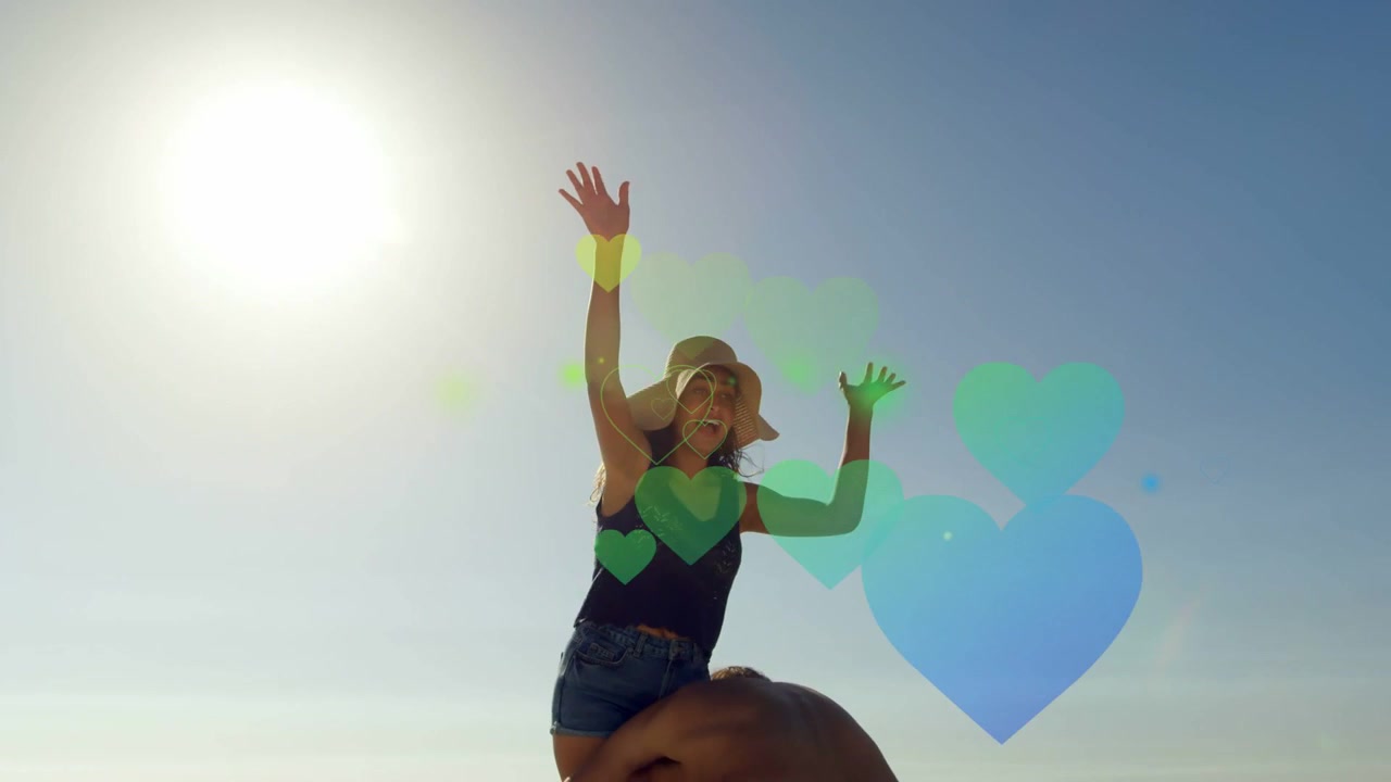 Mulher com os braços erguidos enquanto um homem a levanta e a vira sobre os ombros na praia, com corações em uma campanha de marketing lúdica.