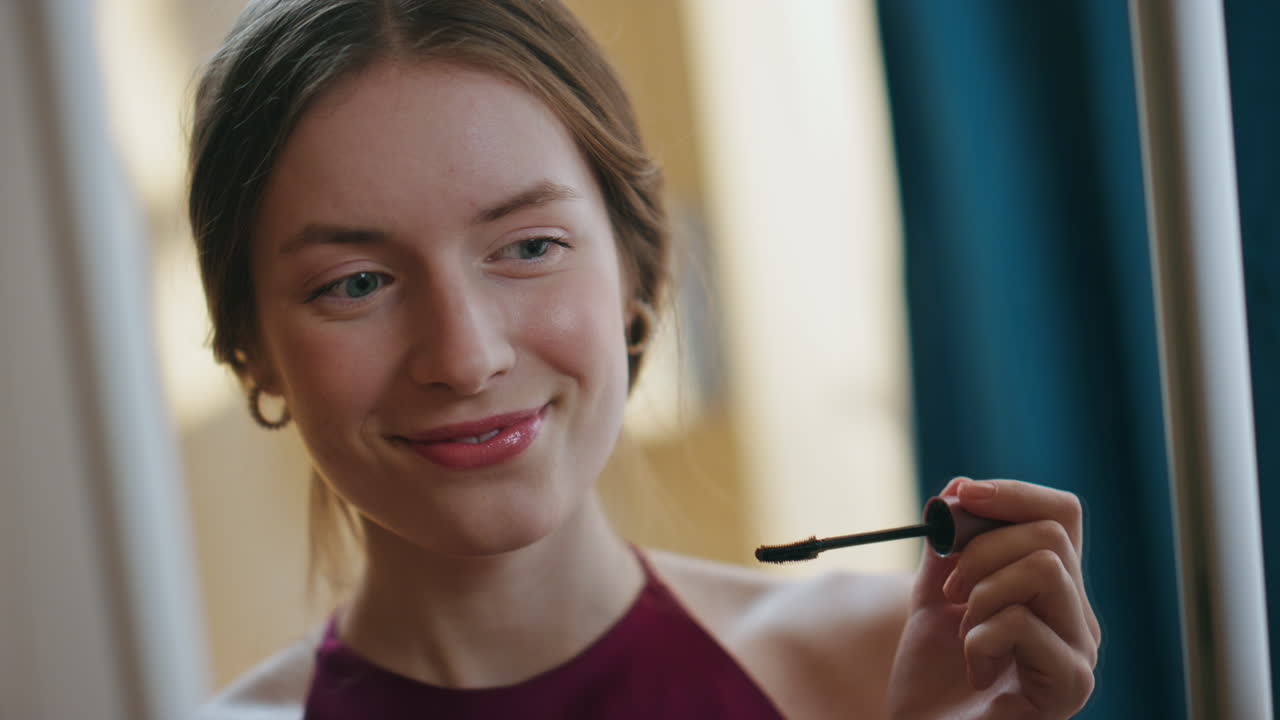 Smiling model applying mascara on eyelashes closeup. Attractive girl admiring