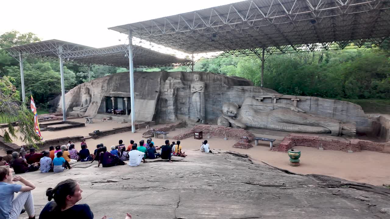 Visitors gather on a viewing platform to enjoy the ancient rock temple of Uththararamaya at Gal Vihara, featuring four magnificent Buddha statues in Polonnaruwa, Sri Lanka.