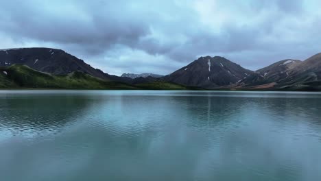 drone low dolly establishing green mossy highland slopes in landmannalaugar, iceland with lake reflection of mountains
