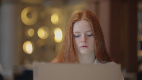 young redhead woman is working with laptop at home or in cafe freelancer or student learning remotely