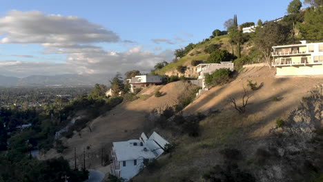 Aerial-flyby-of-homes-on-stilts-hanging-off-cliffs-of-a-mountain-overlooking-a-valley-city