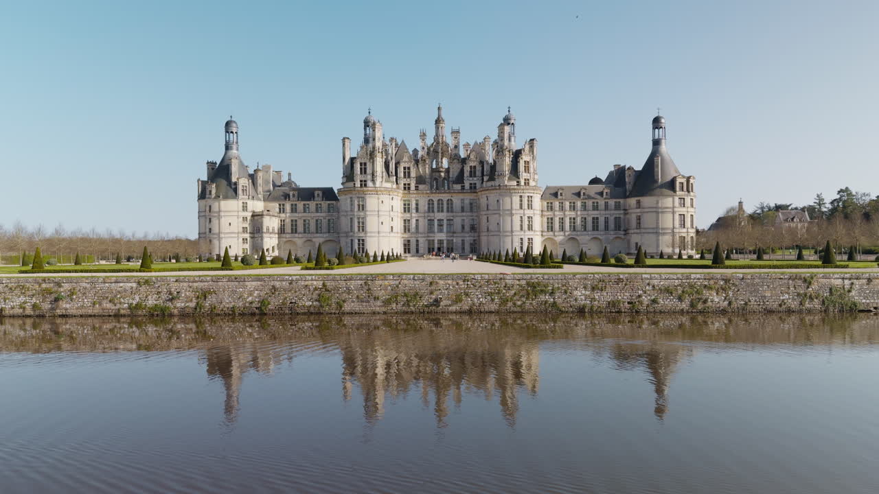 Royal castle of Chambord with canal reflection, tourists, and peaceful sunny weather