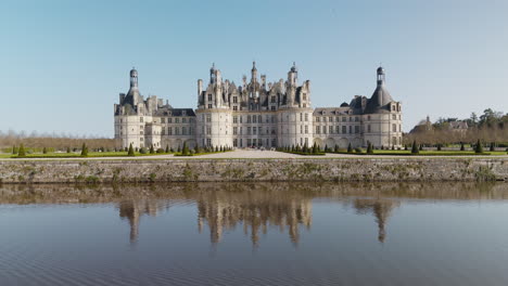 royal castle of chambord with canal reflection, tourists, and peaceful sunny weather