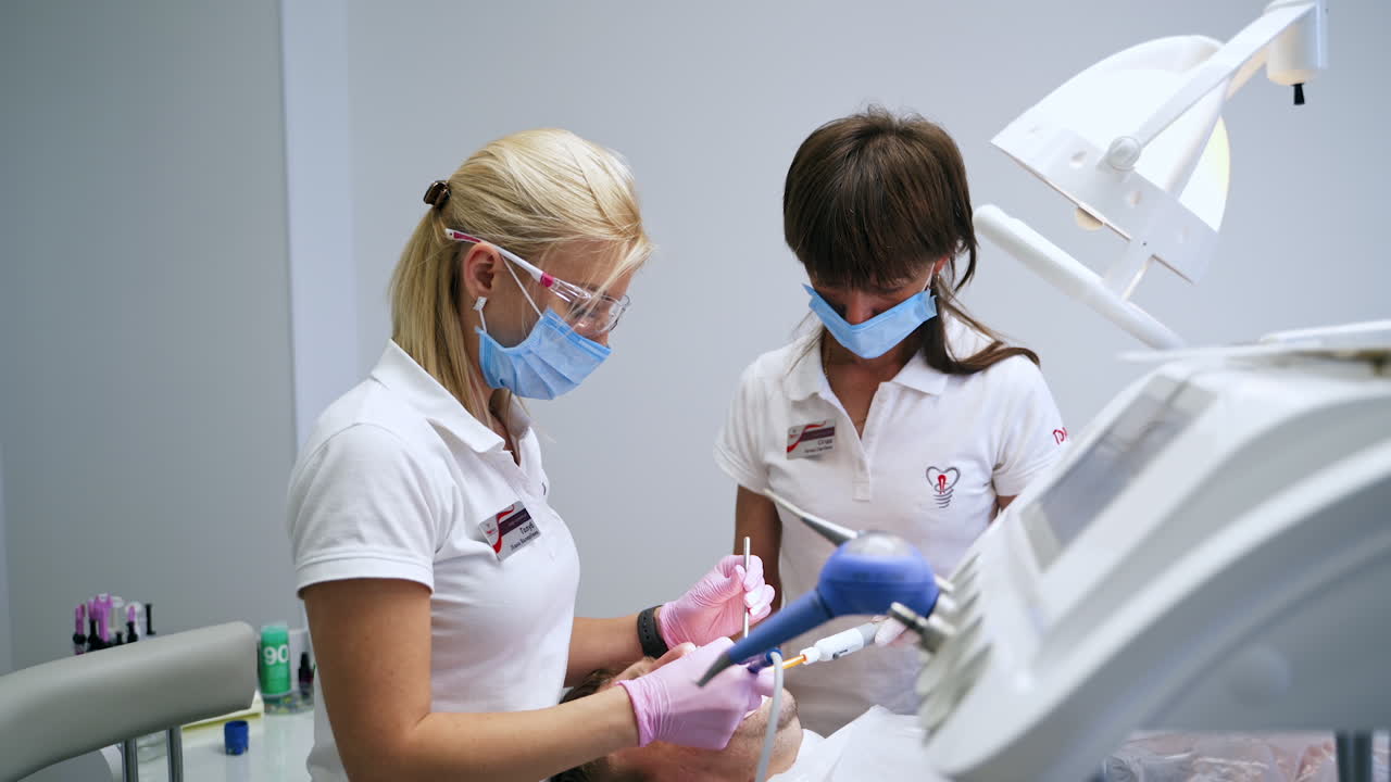 Spacious dentist's cabinet with professionals working in. Female doctor treating teeth with the help of modern equipment.