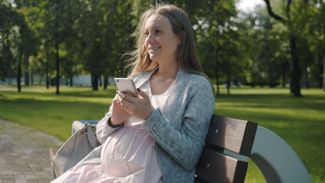 Pregnant woman using mobile phone in a park