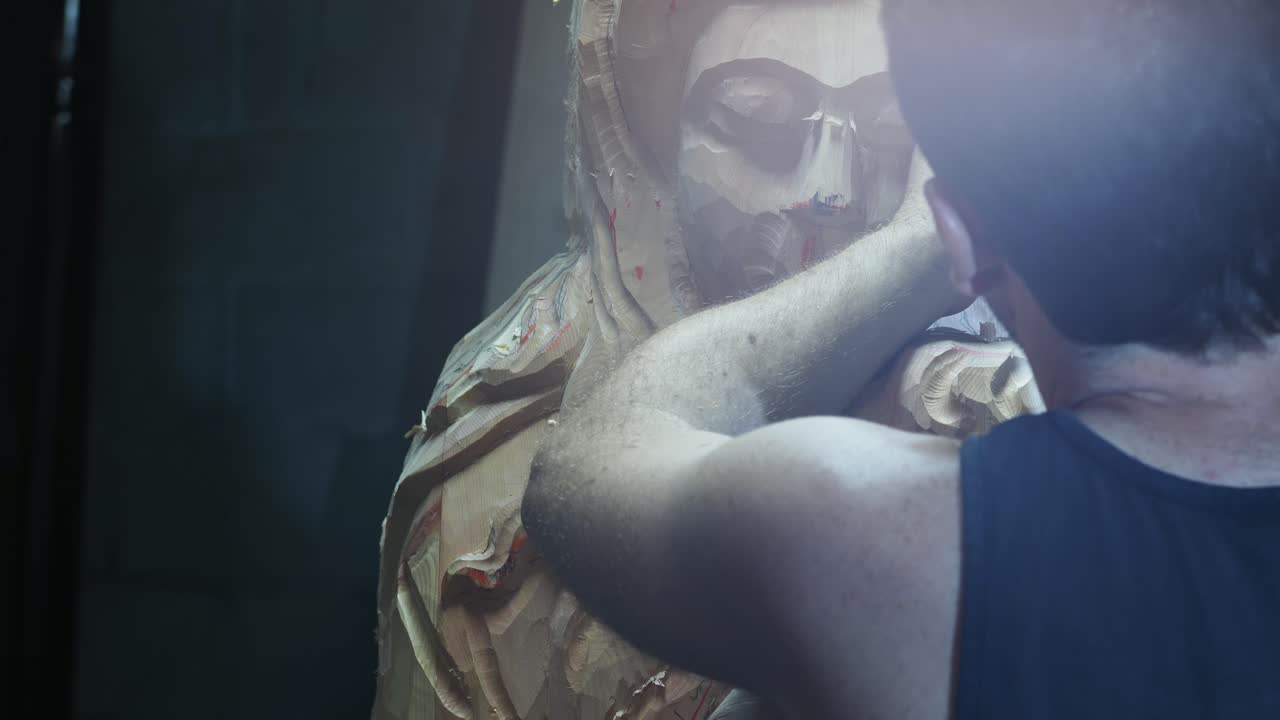 Professional sculptor carefully chiseling intricate details of wooden statue using traditional hand tools in controlled workshop environment, capturing precision of woodworking craft slow motion shot