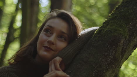 beautiful brunette with dreamy eyes is leaning against a tree trunk surrounded by forest nature