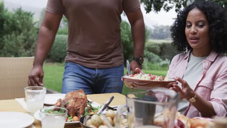 Felices-Padres-Birraciales-E-Hija-Disfrutando-De-La-Comida-En-La-Mesa-En-El-Jardín,-Cámara-Lenta