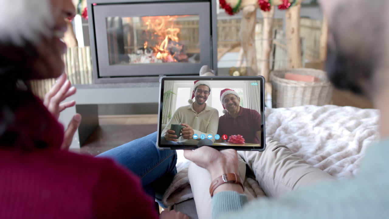 Coppia felice e diversificata, padre e figlio adulto, che fanno una videochiamata di Natale tramite tablet, al rallentatore