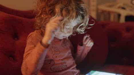 a small girl plays or watches a tablet computer with the light from the screen in a dark room