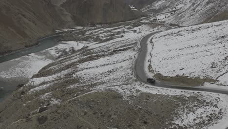 aerial drone view of black suv driving winding snow rocky mountain roads in winter through hunza valley