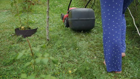 legs of young woman mowing lawn by lawn mower near country house