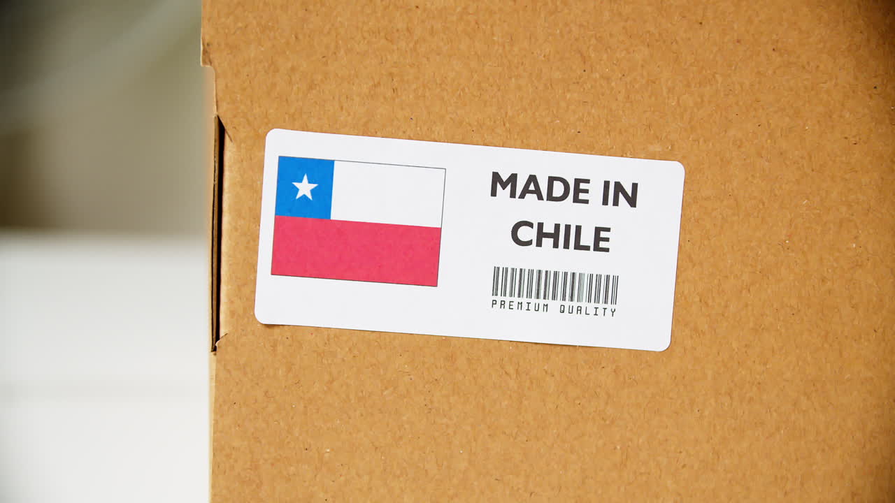 manos aplicando la etiqueta de la bandera hecha en chile en una caja de cartón de envío con productos