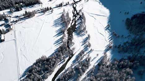 Aerial-view-of-snow-covered-landscape-with-forests-and-rivers-on-a-sunny-winter-day-in-Alp-Grum,-Switzerland