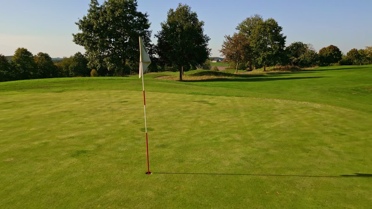 Drone che vola vicino alla bandierina su un green da golf. Ripresa aerea all'indietro, con spazio per il testo.