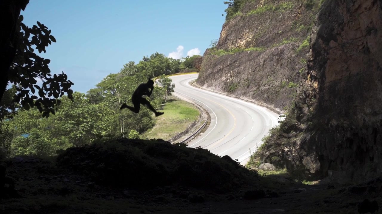 Young men jumping in slow-mo while inside a big cave in siluette with beautiful nature and ocean view in a Caribbean Island road.