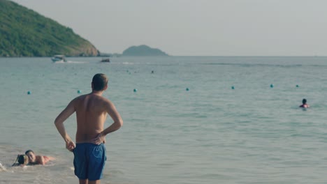 man-looks-at-family-playing-in-rolling-waves-at-ocean-beach