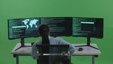 vista trasera de una desarrolladora asiática con dolor de espalda mientras escribe código con múltiples pantallas de computadora en el estudio de pantalla verde
