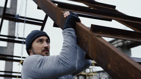 joven deportista guapo haciendo pull-ups en la construcción de metal en las ruinas de una fábrica abandonada en una mañana nublada