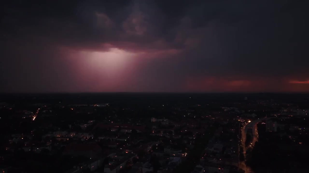 Lyn oplyser mørk nattehimmel over byens bygninger, der fanger den dramatiske kraft fra et sommertordenvejr. Fantastisk luftfoto med roterende panorering mod venstre fra drone.
