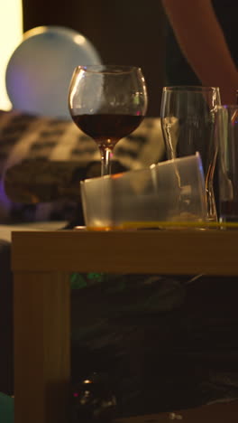 Vertical-Video-Close-Up-Of-Person-Clearing-Up-Bottles-And-Glasses-From-Messy-Lounge-Or-Living-Room-After-House-Party