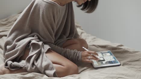 woman drawing on tablet in bed