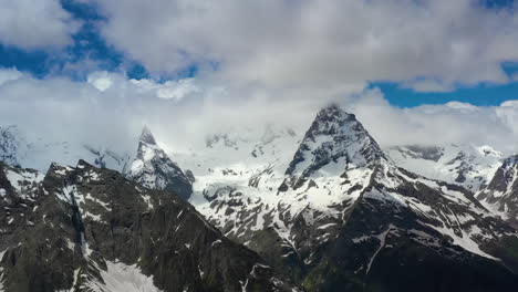 Air-flight-through-mountain-clouds-over-beautiful-snow-capped-peaks-of-mountains-and-glaciers.