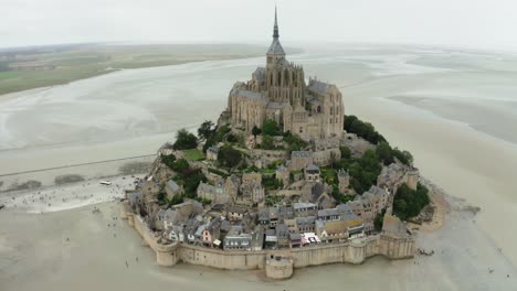 Cámara-Drone-Mont-Saint-Michel-Tomando-Cinemáticas-Tomadas-Desde-El-ángulo-Superior,-Muchos-Jardines-Al-Lado-Del-Edificio