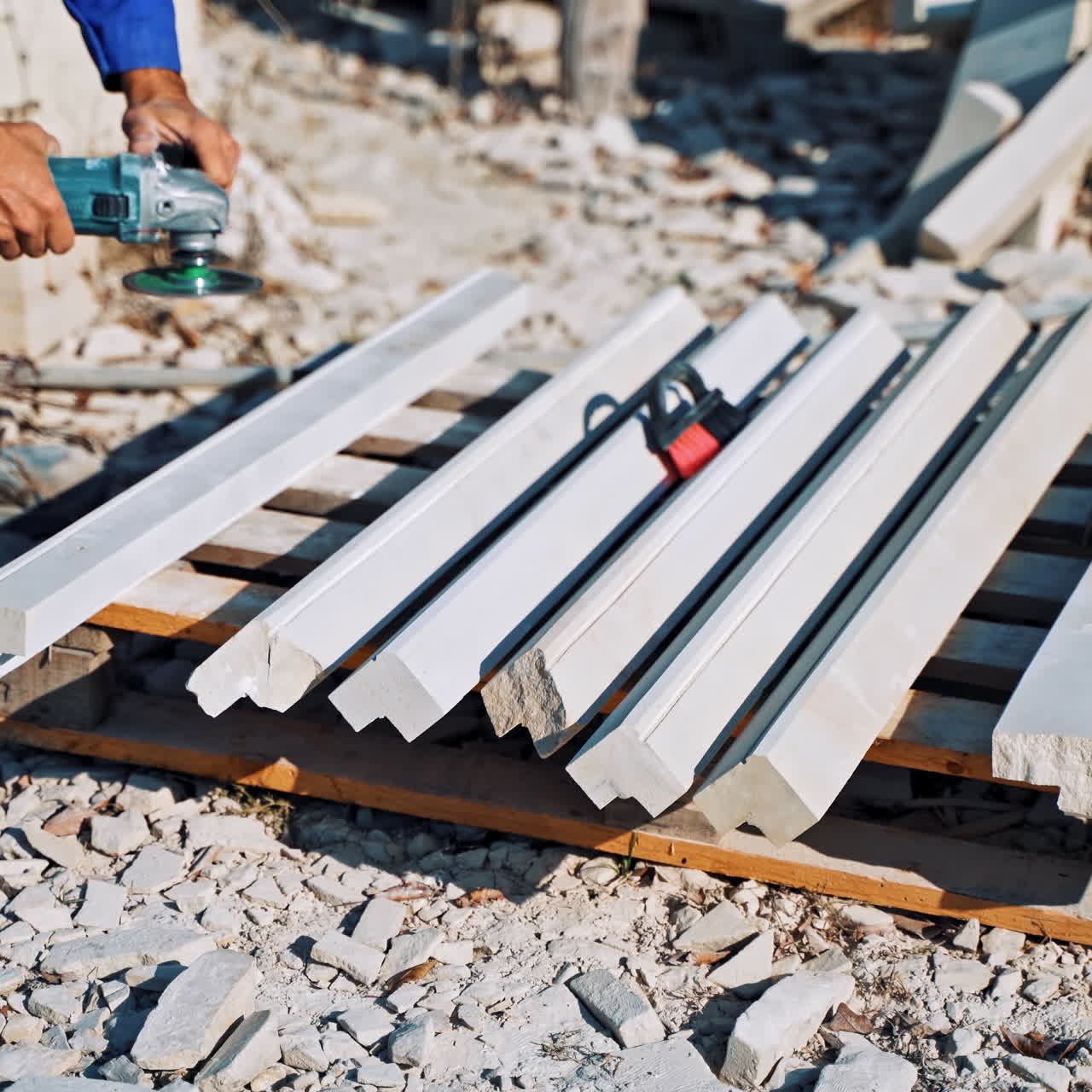 Worker is polishing stone by hand grinder outdoors. Laborer in working clothes grinding stones on the ground.
