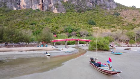 Aerial-Close-Up-shot-of-Colorful-Fishing-boats-on-sand-of-tropical-bay-at-low-tide-with-rocks-on-the-background-in-Thailand