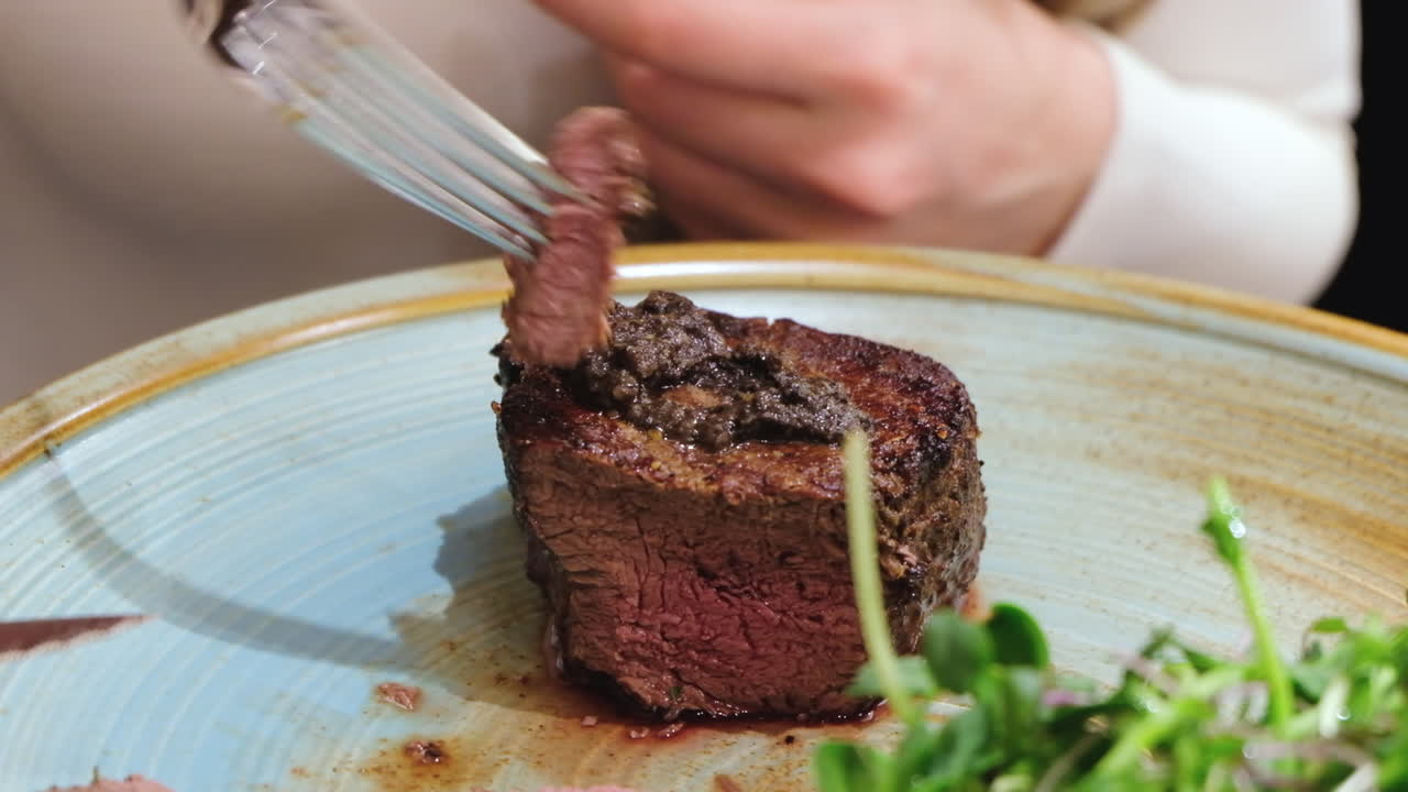 Close up of a woman cutting a piece of filet mignon at a restaurant