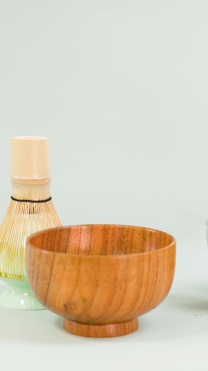 Air dituangkan ke dalam matcha, lalu dikocok dalam mangkuk kayu dengan pengocok bambu, latar belakang bersih minimalis