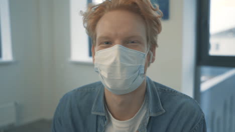 portrait of young handsome redhead man talking to camera with face mask indoor