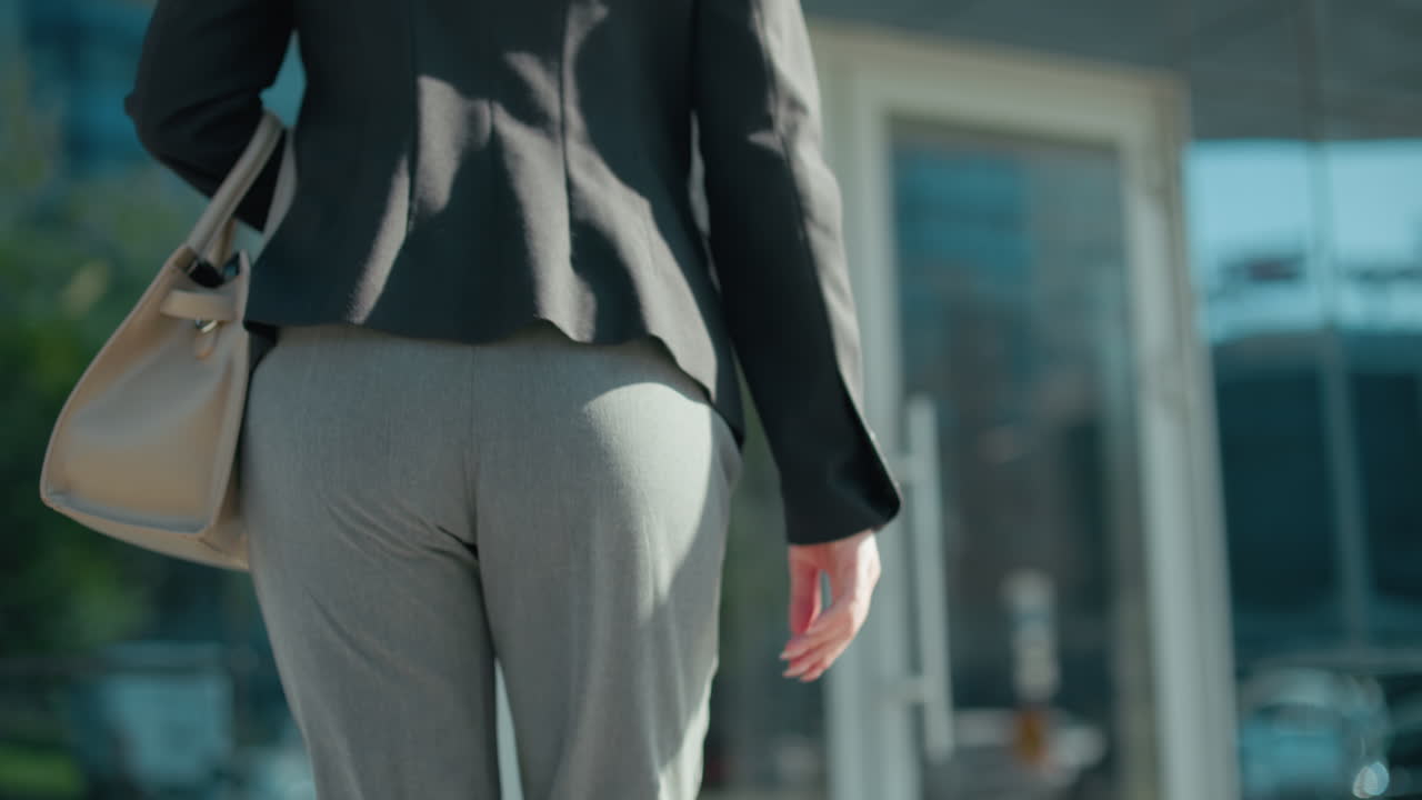 Back view of lecturer walking toward lecture building entrance with glass door handle reflecting busy urban street, cars, and modern cityscape, focus on movement in professional setting outdoors