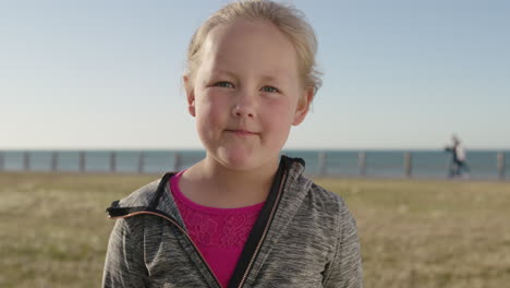 close up portrait of cute little blonde girl looking pensive serious at camera carefree child seaside park