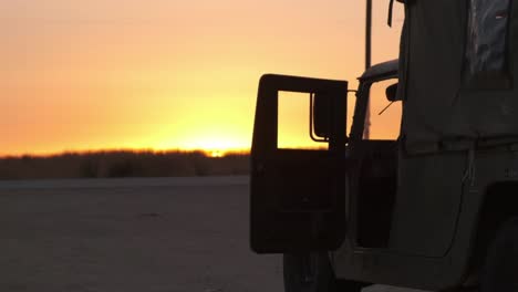 military army hummer vehicle in the middle of the desert during the amazing orange sunset next to a field