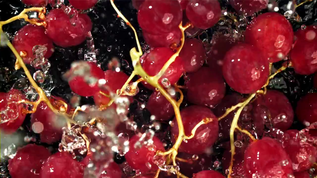 Primo piano di uva rossa che viene lavata con acqua che schizza