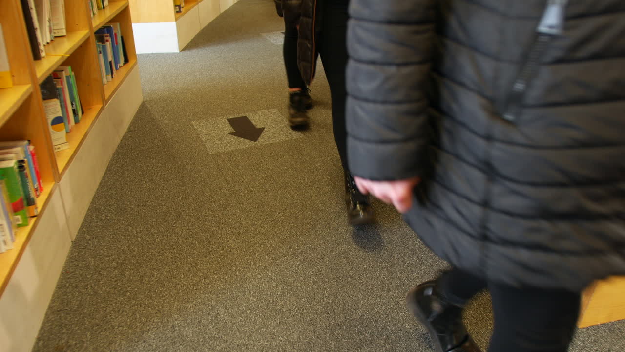 gente caminando por una biblioteca siguiendo las flechas en el suelo