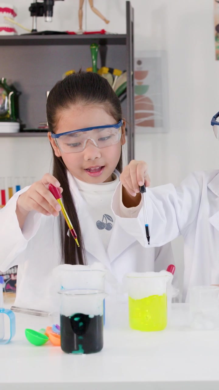 Kaksi nuorta aasialaista tyttöä laboratoriotakeissa ja suojalaseissa käyttämässä pipettejä kemian kokeissa.