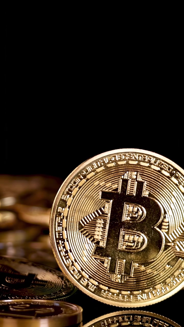 Uma moeda de Bitcoin dourada cai sobre uma pilha de moedas, iluminada por iluminação de estúdio dramática.