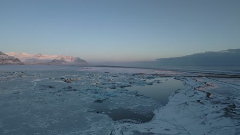 Aerial,-frozen-lake-during-winter,-mesmerizing-mountains-in-background-at-sunset