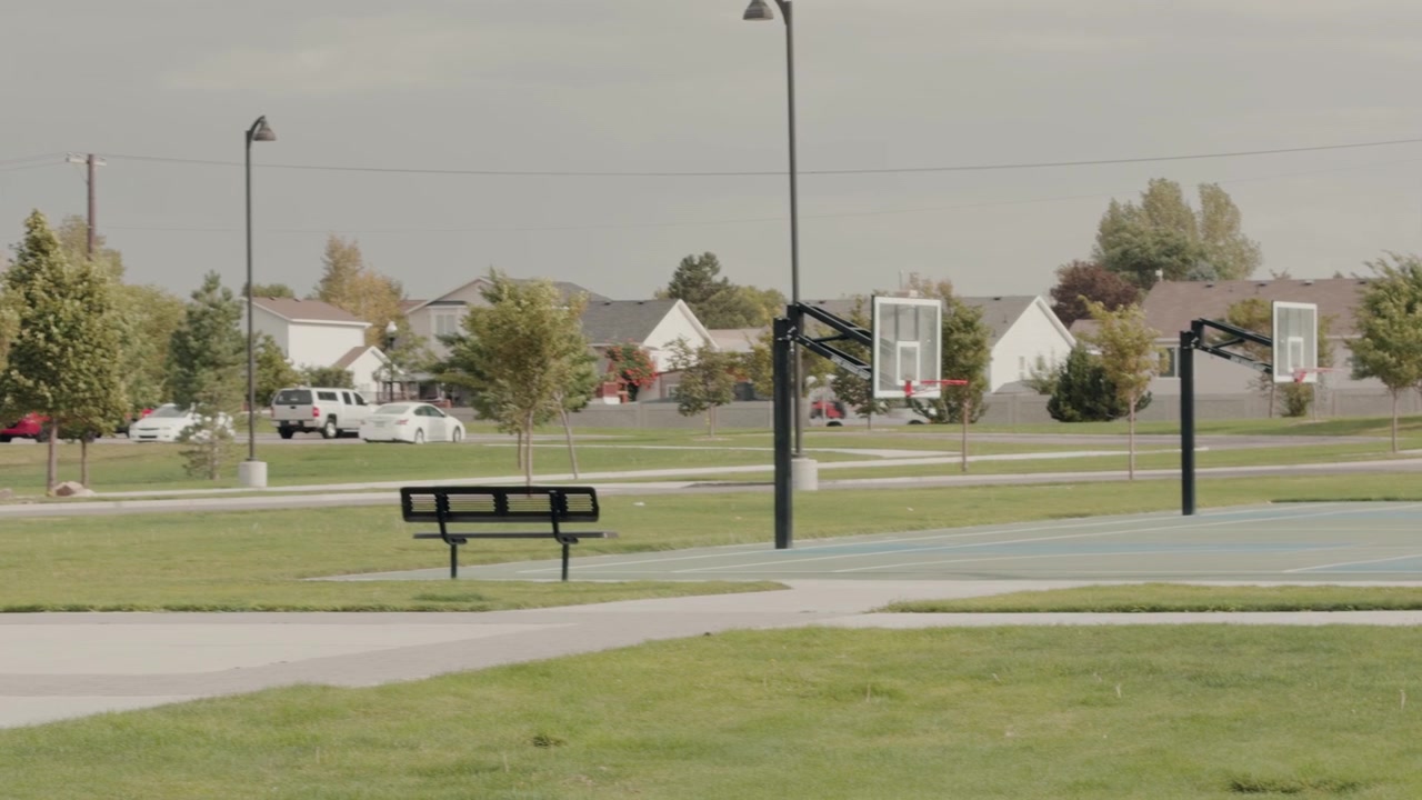 Distant view of a bench and basketball court with parked cars and traffic behind