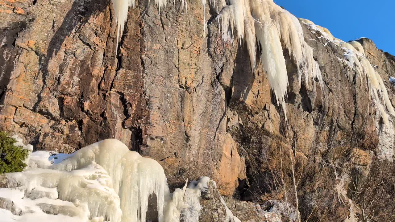 Paljon massiivisia jääpuikkoja sulamassa kevätauringossa vuorenrinteellä kirkkaan sinisen taivaan alla. Video on kuvattu 60 kuvaa sekunnissa, ja se on 23,976 kertaa hidastettu, joten voit päättää, miten haluat käyttää sitä.